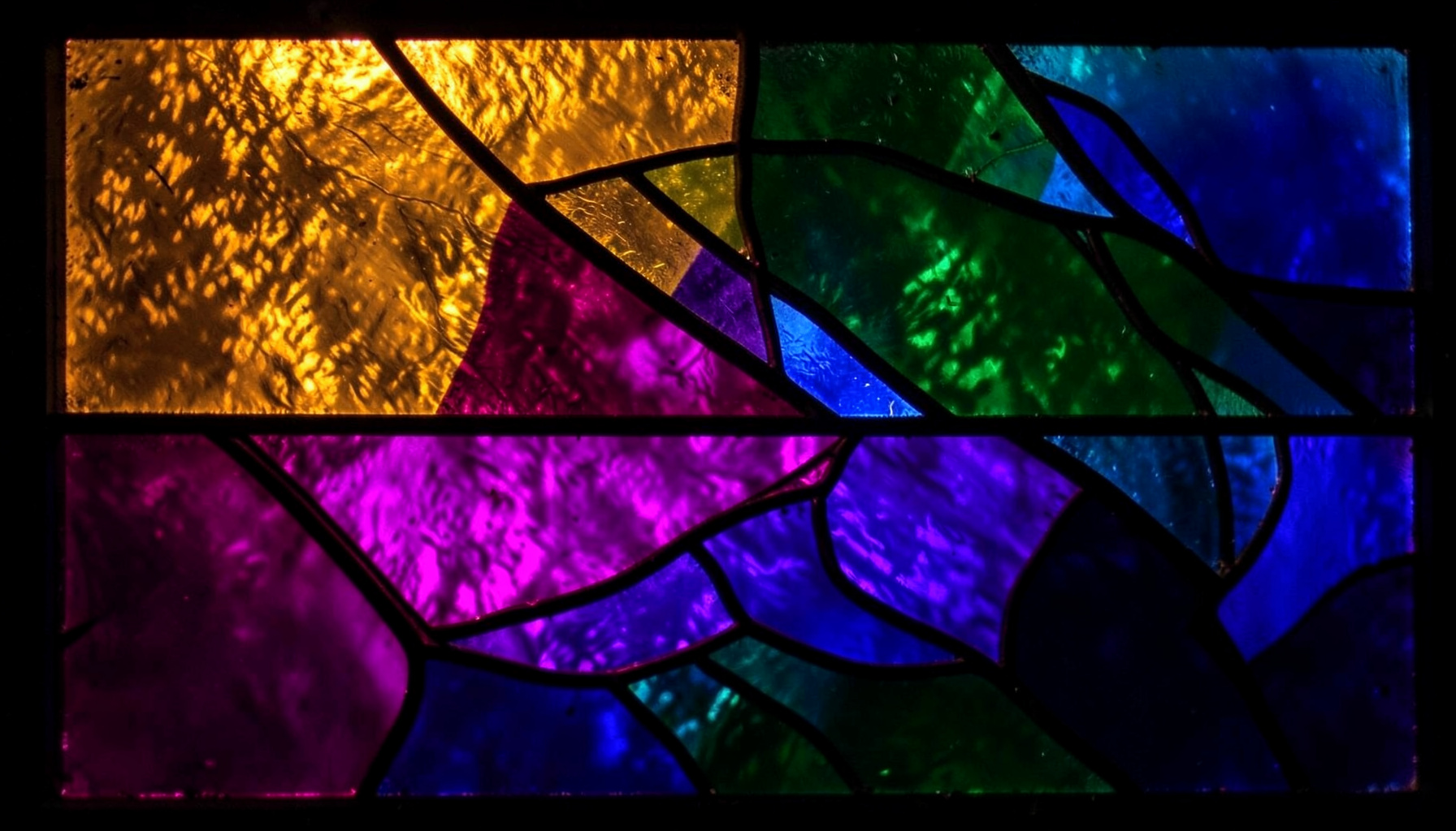 A stained-glass composition with bold leaded segments in deep amber, forest green, and cobalt blue, evoking a warm, wanderlust mood.